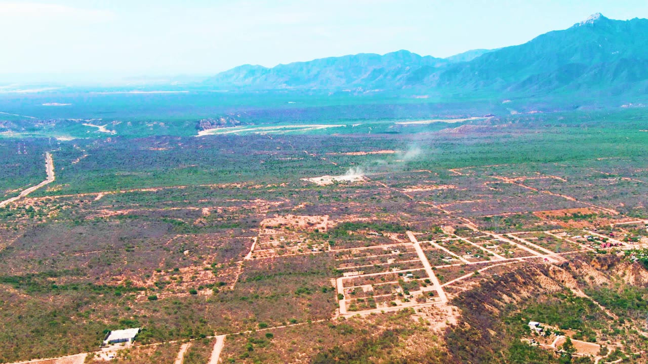 Aerial frame of rural Caduano land with smoke, roads, and mountains.