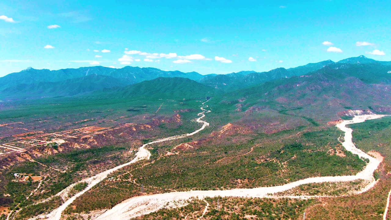 Wide aerial view of a curving road through scrubby terrain and mountains.