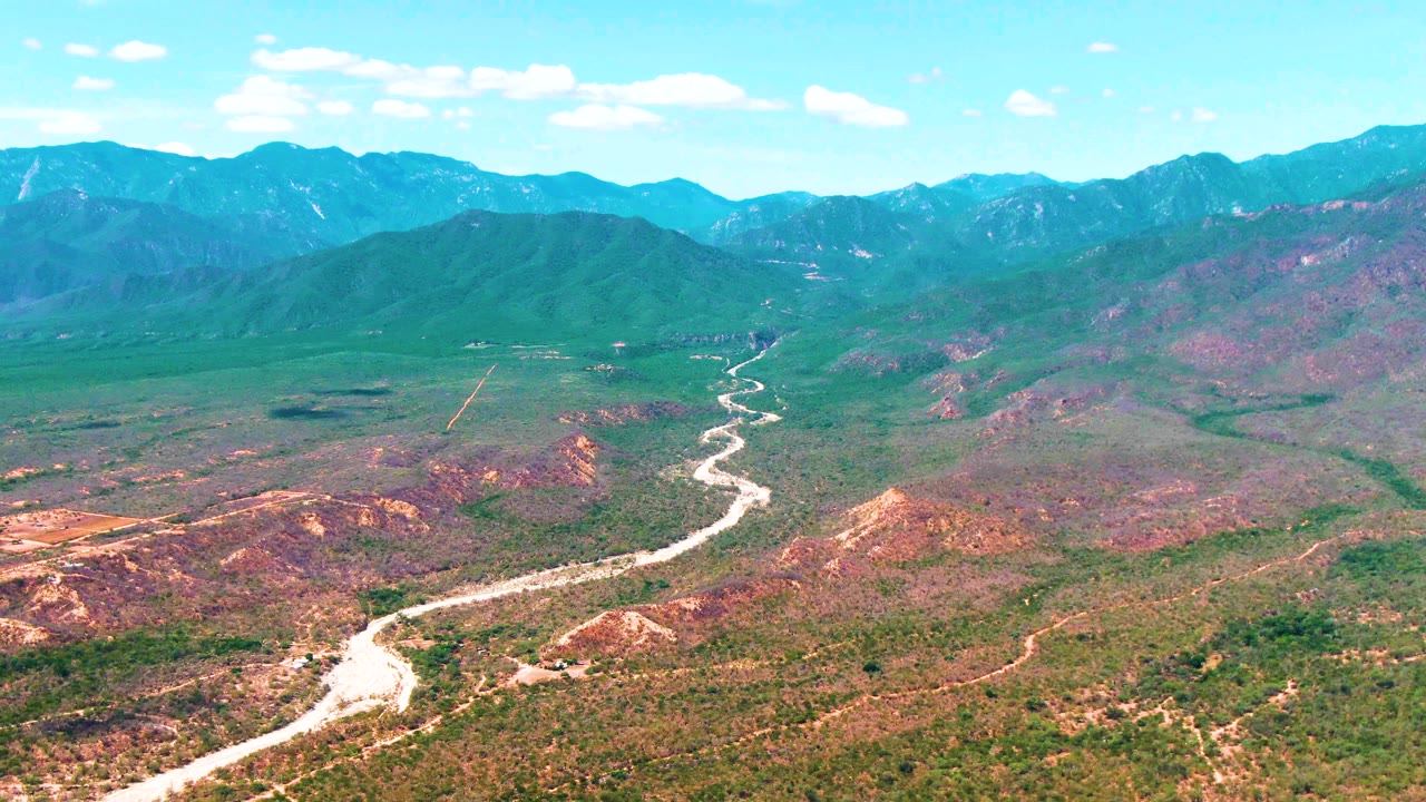 Aerial view of the Caduano landscape where the winding road runs through the center of the valley, bordered by green scrub and reddish earth, with no visible people.