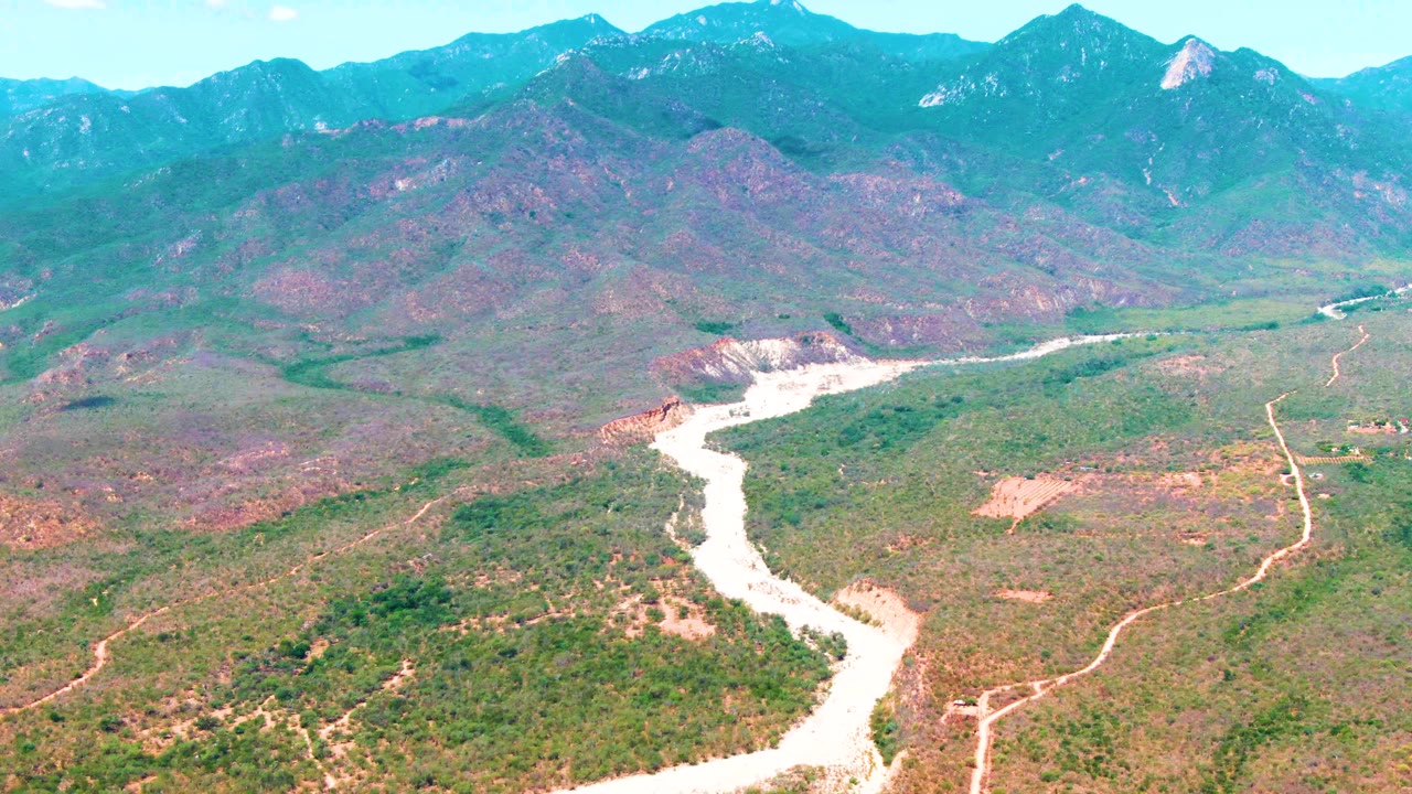 Drone view of a winding river below a mountain range and bright sky.