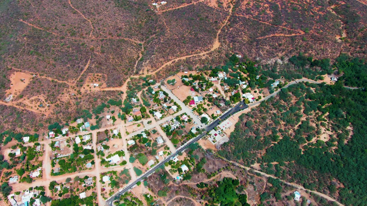 Drone view of houses and a diagonal road bordered by trees and scrub terrain.