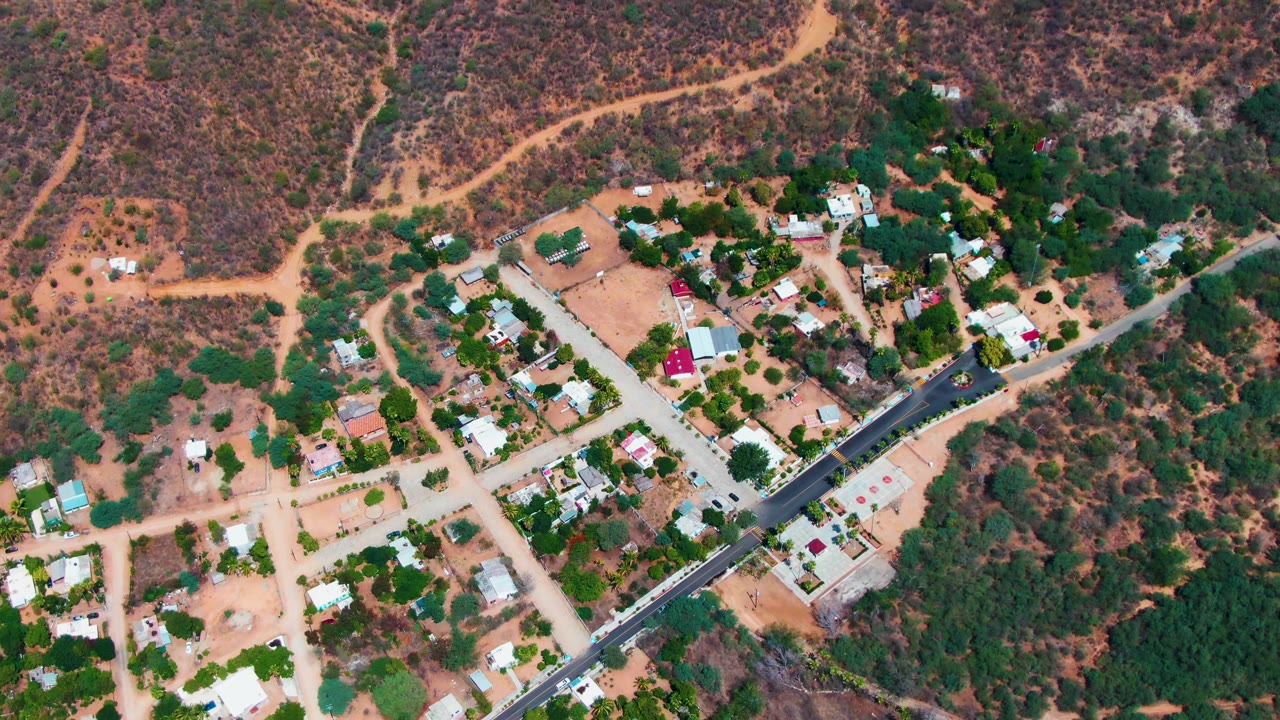 Aerial view of homes and trees below winding dirt tracks on a hillside.