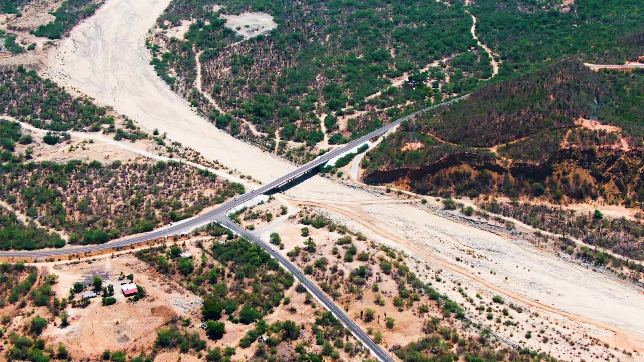 Aerial frame from Caduano, Baja California Sur, centering the bridge and intersecting road over the dry riverbed with hills, desert scrub, and no visible people.