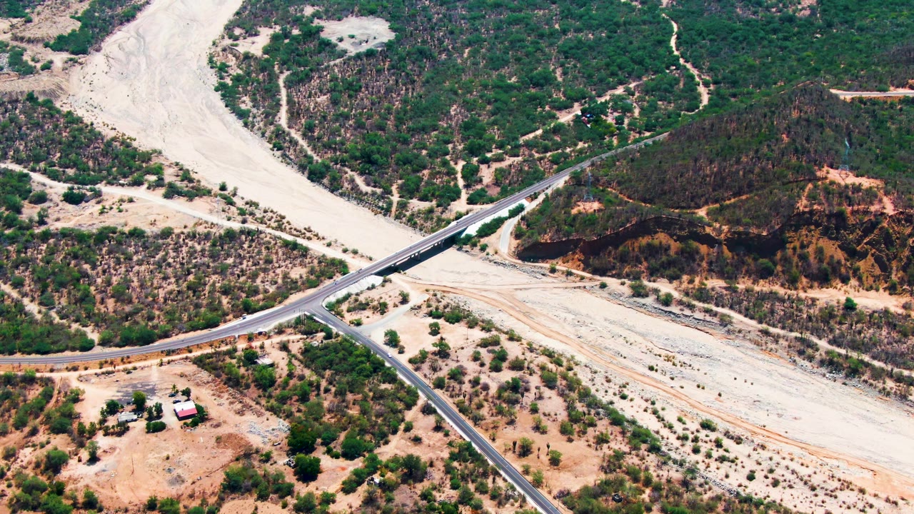 Aerial road junction with dry riverbed and scattered buildings nearby.