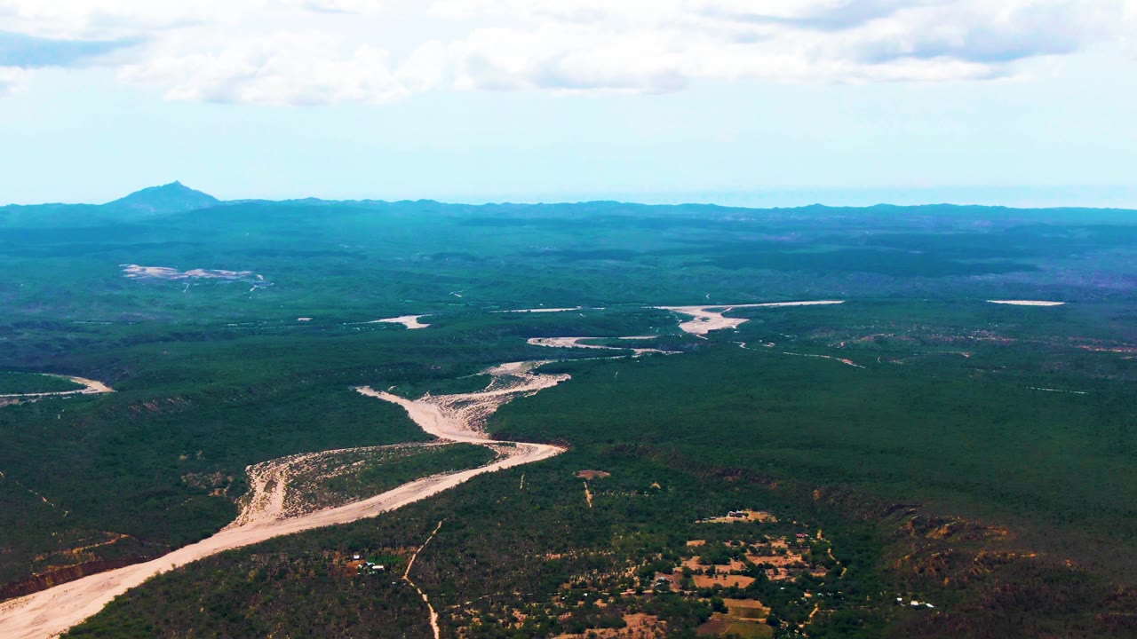 At 0:01, the Caduano aerial view keeps the sandy riverbed prominent in the lower frame as it branches through forest and low hills, with no visible people.