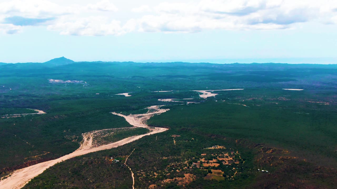 At 0:02, pale bends of the river lead from the foreground into the Caduano forested valley, with distant ridges beneath a bright cloud layer and no visible people.
