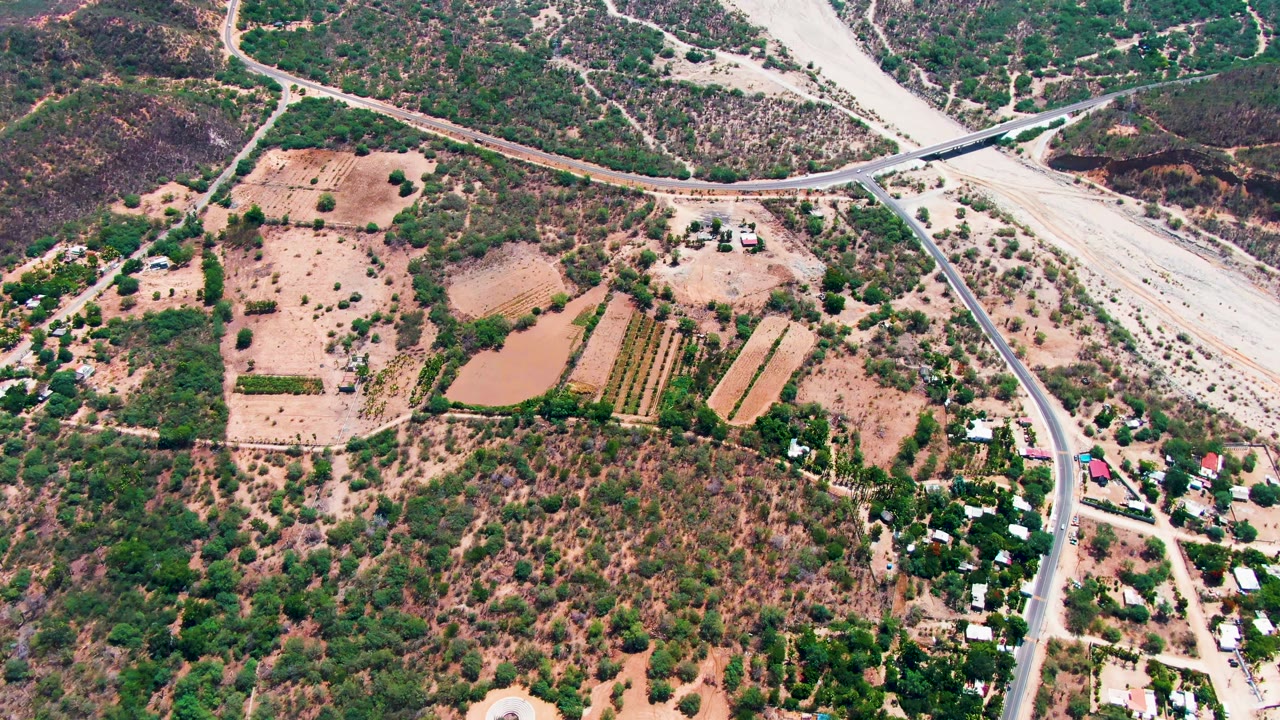 Aerial rural landscape with road, bridge, dry wash, fields, and clustered buildings.