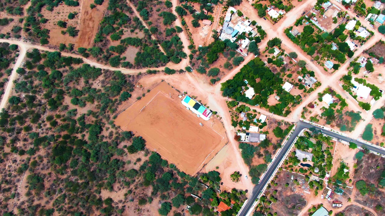 Aerial view of dirt roads crossing a dry settlement near trees and homes.