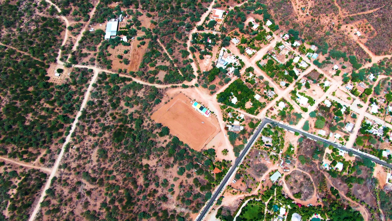 Top-down residential area with dirt roads, homes, trees, and dry scrubland.