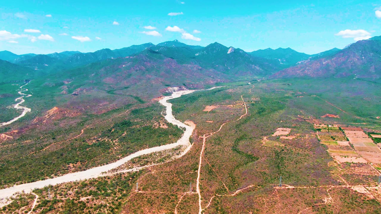 Drone view across a river valley with mountains and scattered white clouds.