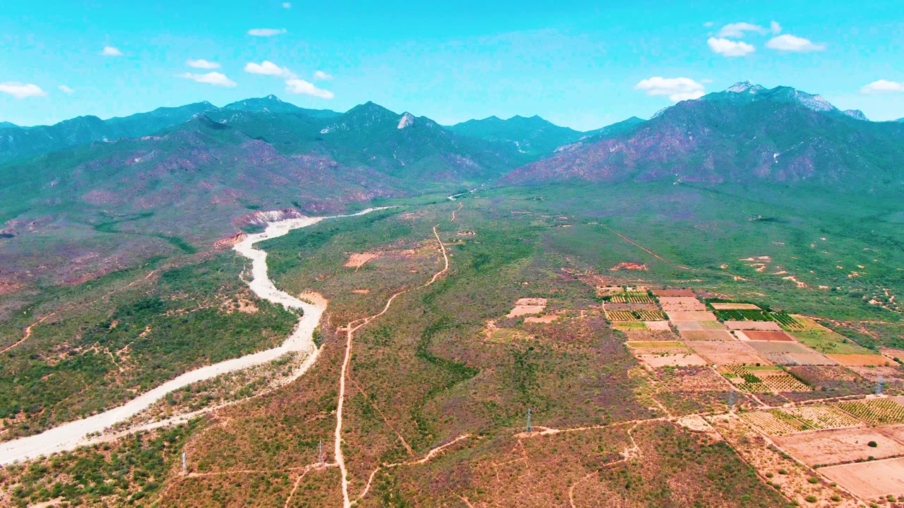 Winding river beside dirt tracks and rectangular fields in a mountain valley.