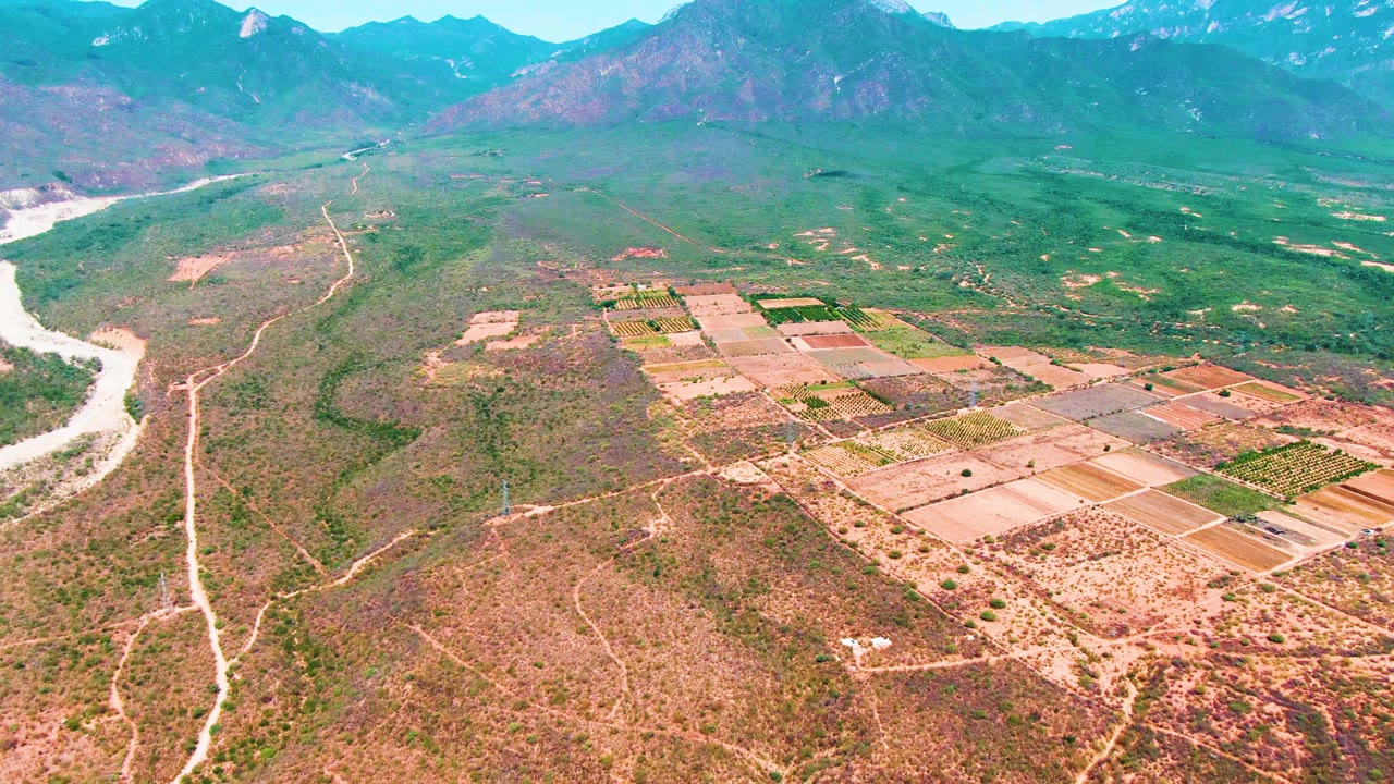 Aerial view of farmland, scrubland, river channel, and mountains.