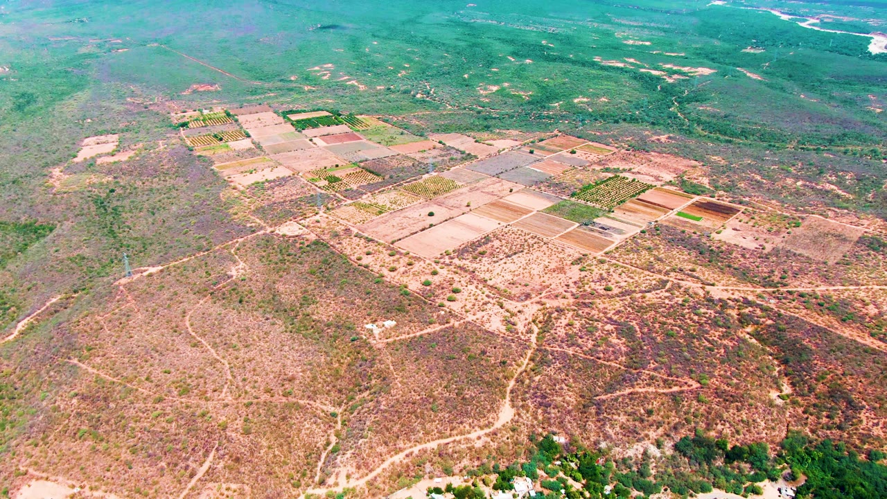 Caduano aerial frame showing tan tilled fields, small green crop sections, branching dirt roads across rough dry land, and a river corridor near the top of frame, no visible people.