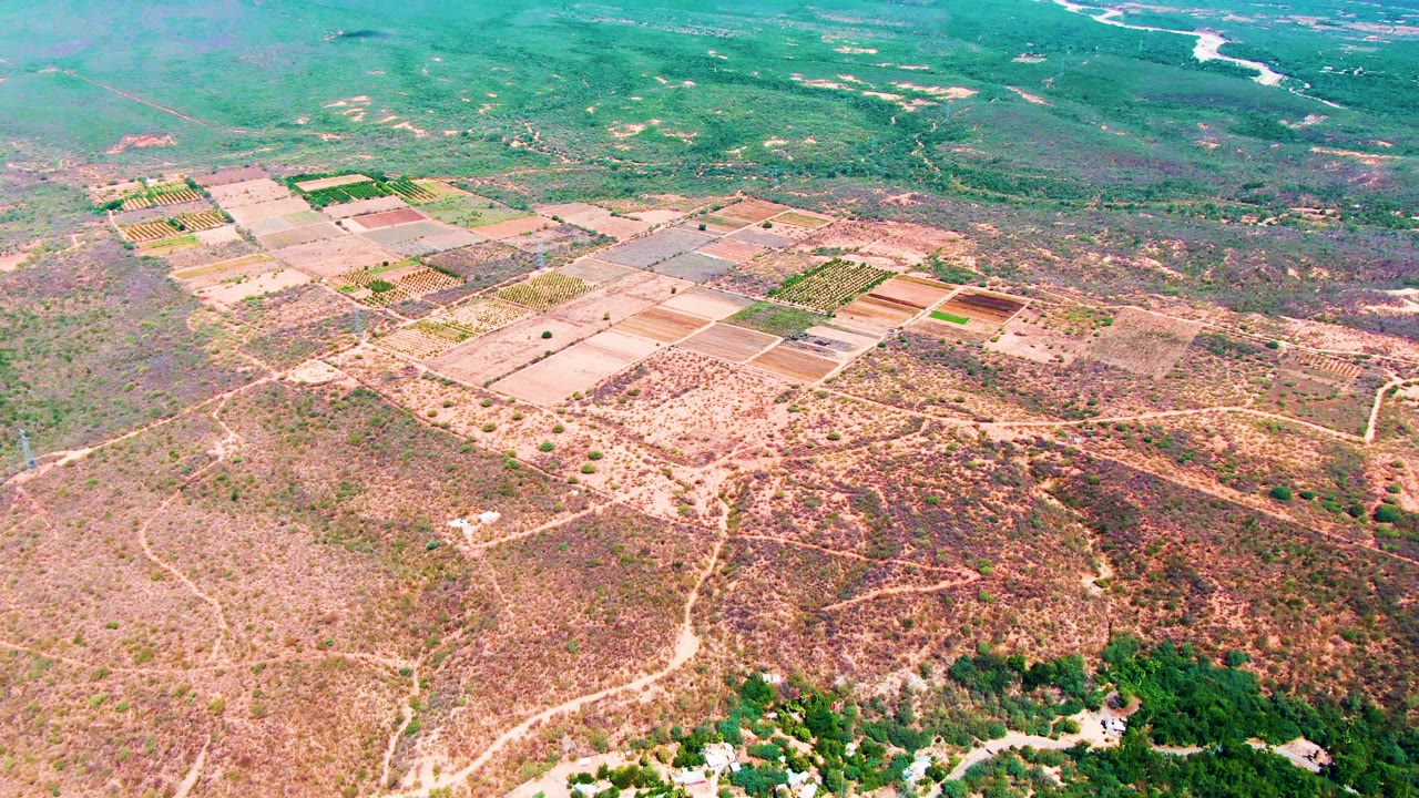 Aerial view of tilled fields, dirt tracks, dry scrubland, green hills, and a distant river valley.