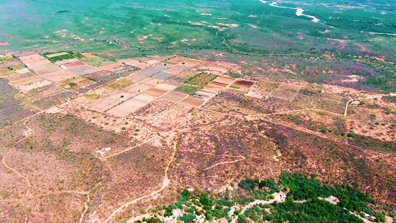 Caduano aerial frame with rectangular fields near the upper left, arid valley floor across the foreground, a green hillside edge below, and no visible people.