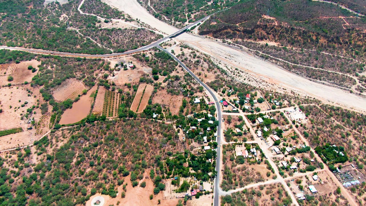 Aerial frame over Caduano, Baja California Sur, Mexico showing intersecting rural roads, tan fields, scrub-covered hillsides, scattered buildings, and no visible people.