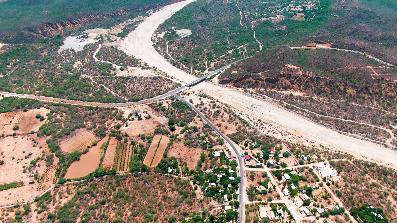Drone view of a winding dry river channel beside fields and roads.