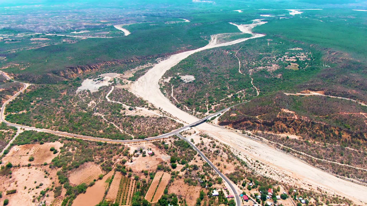Aerial landscape with a pale river channel, green hills, bridge, and farm plots.