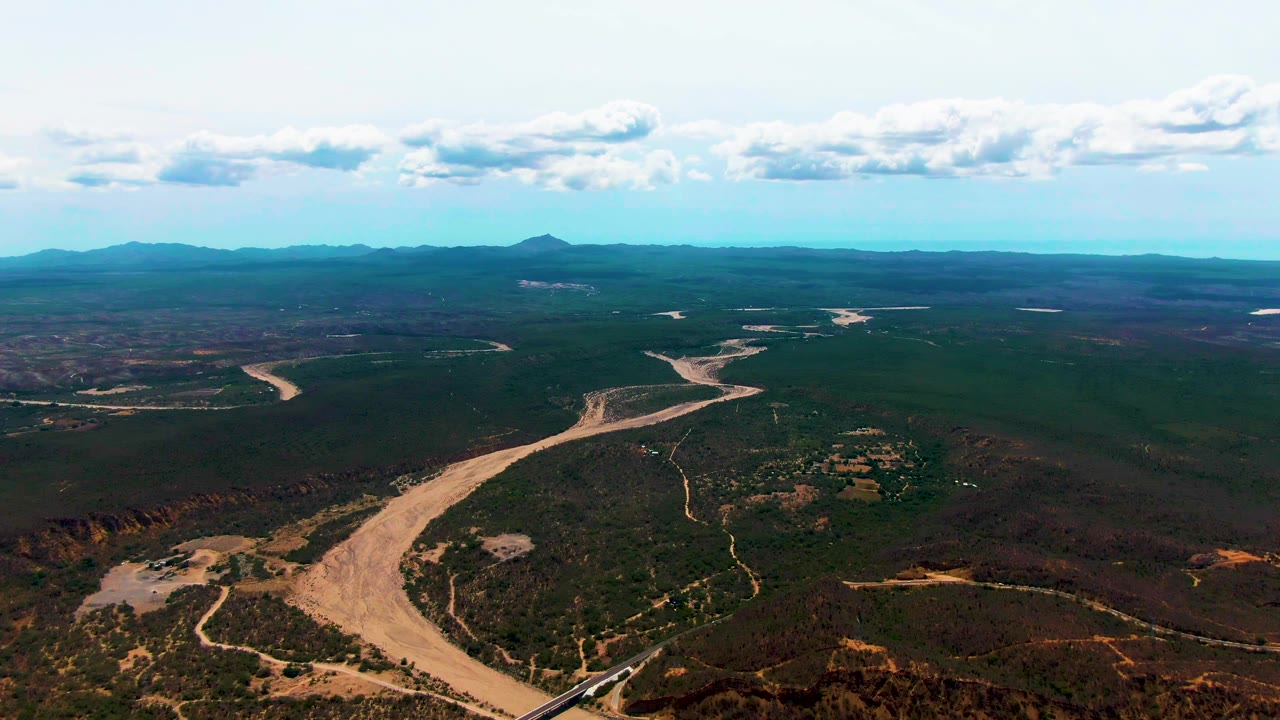 Aerial view of winding river, rail line, scrub terrain, and distant mountains.