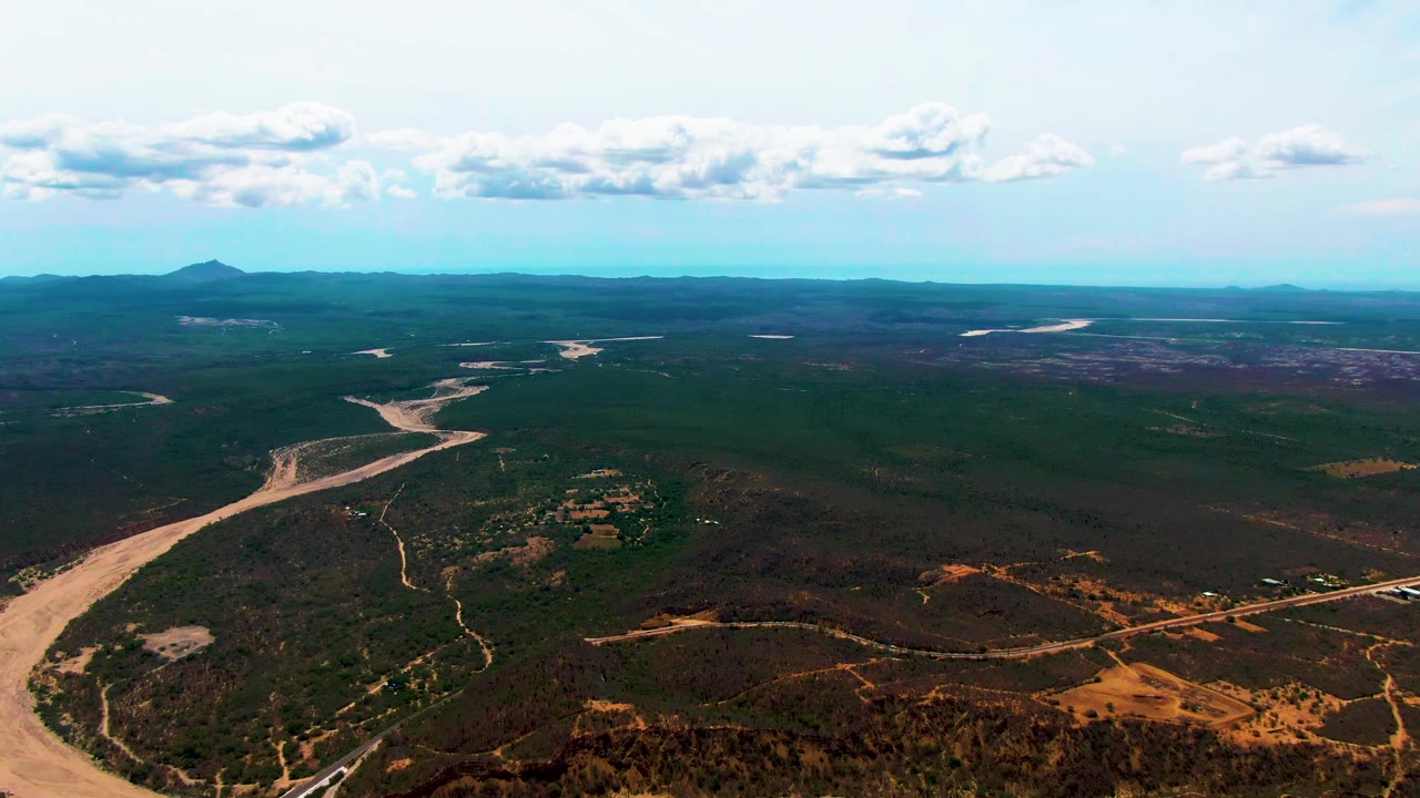 Wide aerial view of a winding pale river channel through green and brown terrain