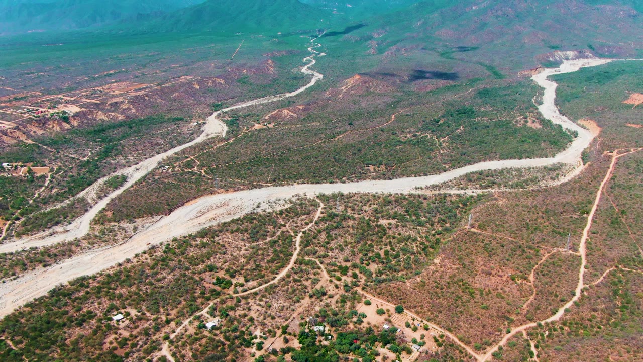 Aerial view of winding dry channel or road crossing scrubby desert hills.