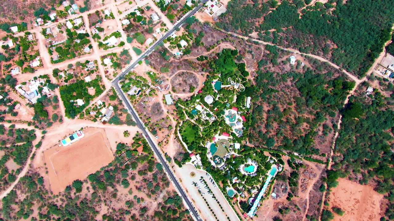 Overhead road and pool property bordered by trees and dry open land.