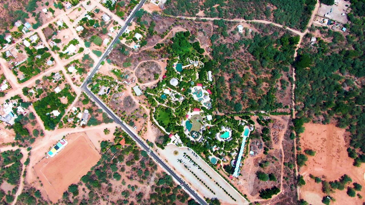 Overhead neighborhood scene with dirt lots, a paved road, trees, and swimming pools.