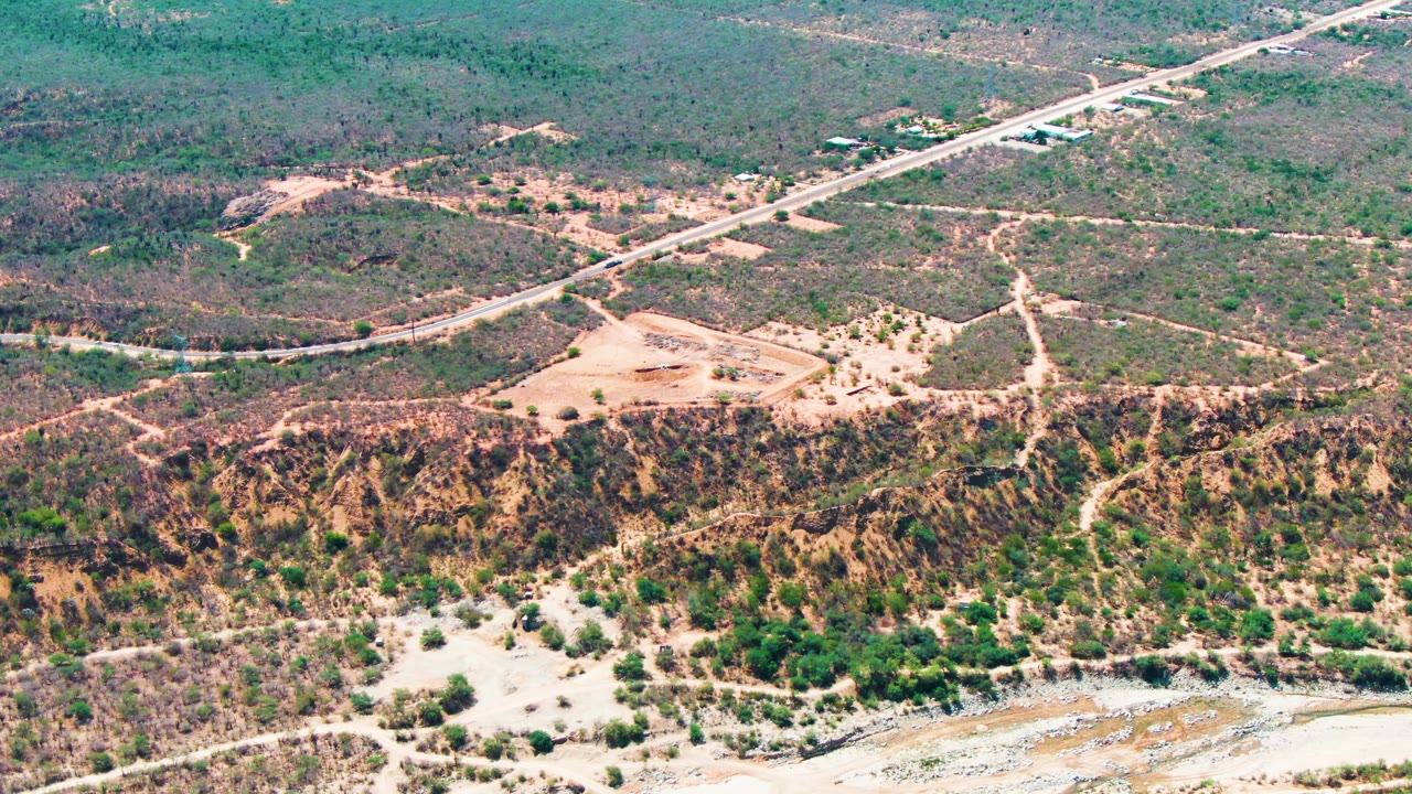 Aerial frame from Caduano, Baja California Sur with pale dirt tracks branching through scrubland below the main road, an eroded hillside, and no visible people.