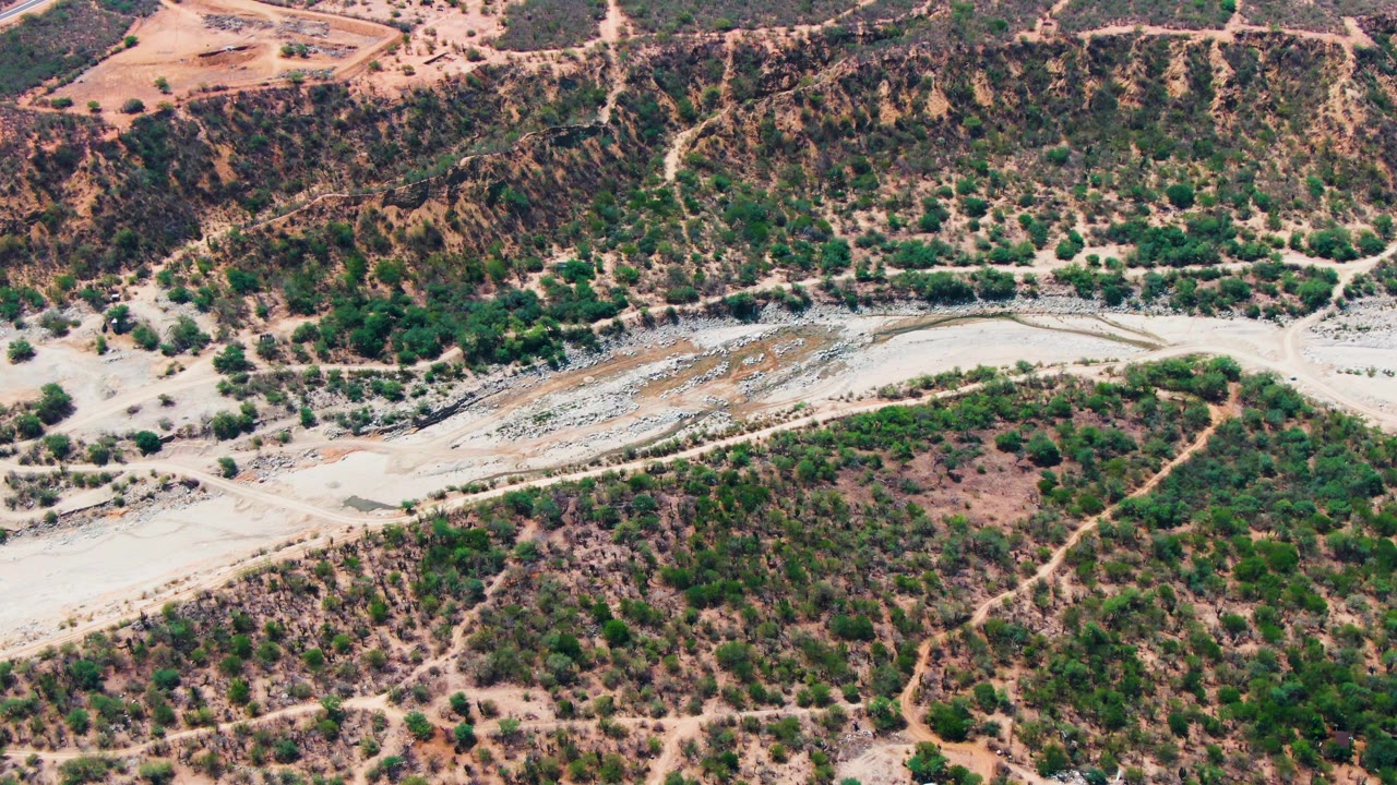 Dry wash crossing a rugged slope with scattered green vegetation.