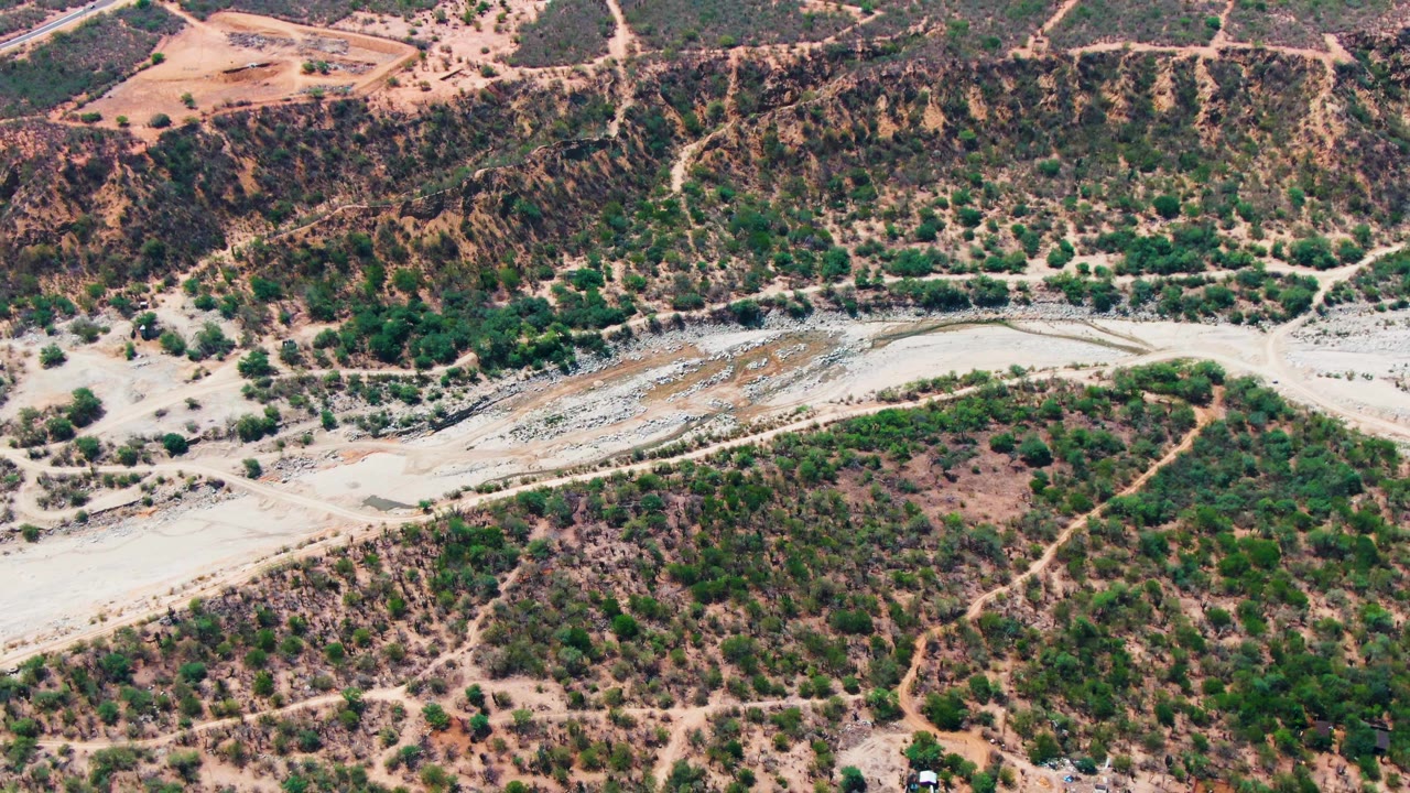 Aerial landscape with a dry channel below a scrub-covered ridge.
