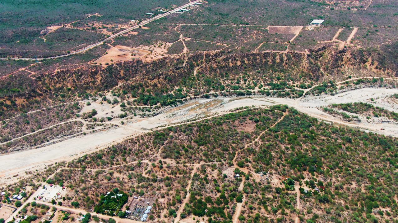 Aerial frame over Caduano, Baja California Sur, with the dry wash running across the middle, greener vegetation clustered near low areas, dirt roads above, and no visible people.