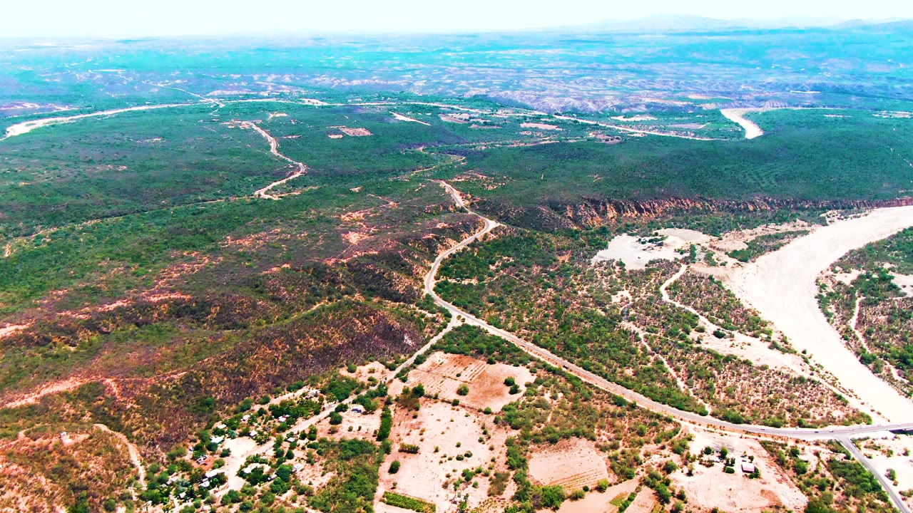 Aerial view of a road, riverbed, and patchy vegetation across dry hills.