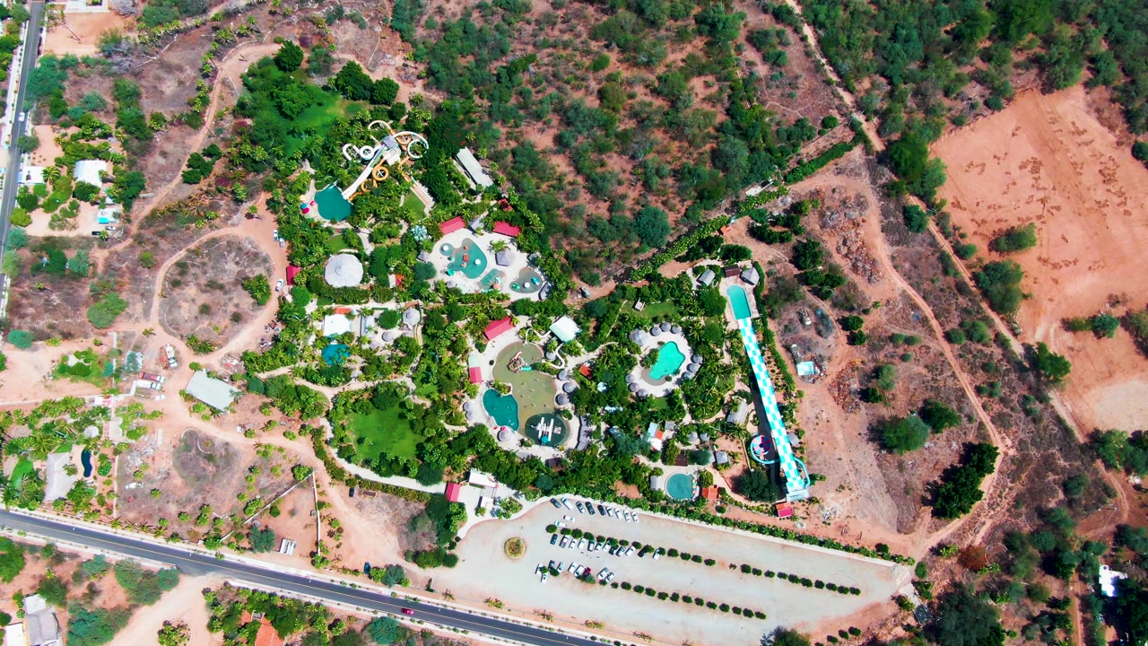 Resort complex from above with pools, trees, slide area, parked cars, and dry terrain.