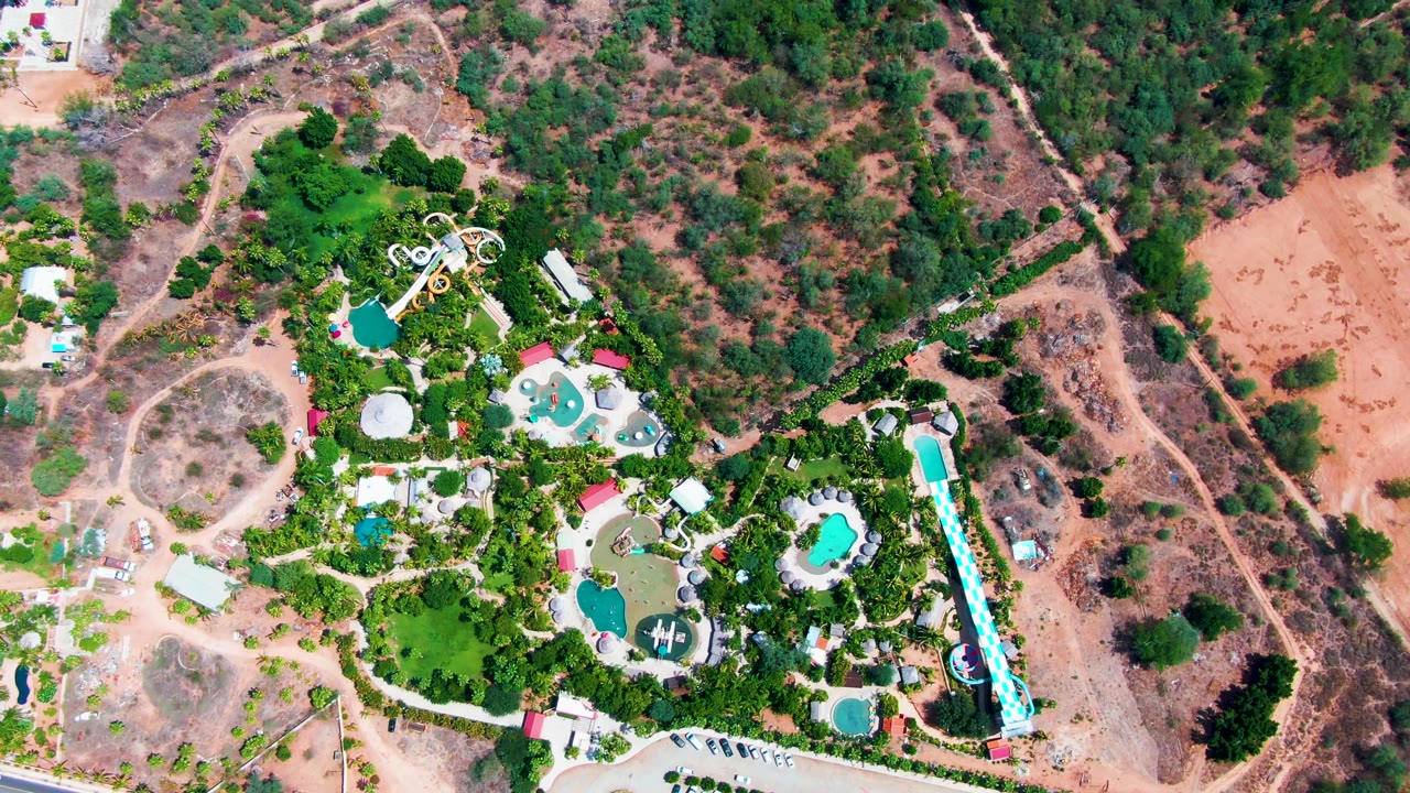 Aerial resort grounds with pools, trees, and scrubland