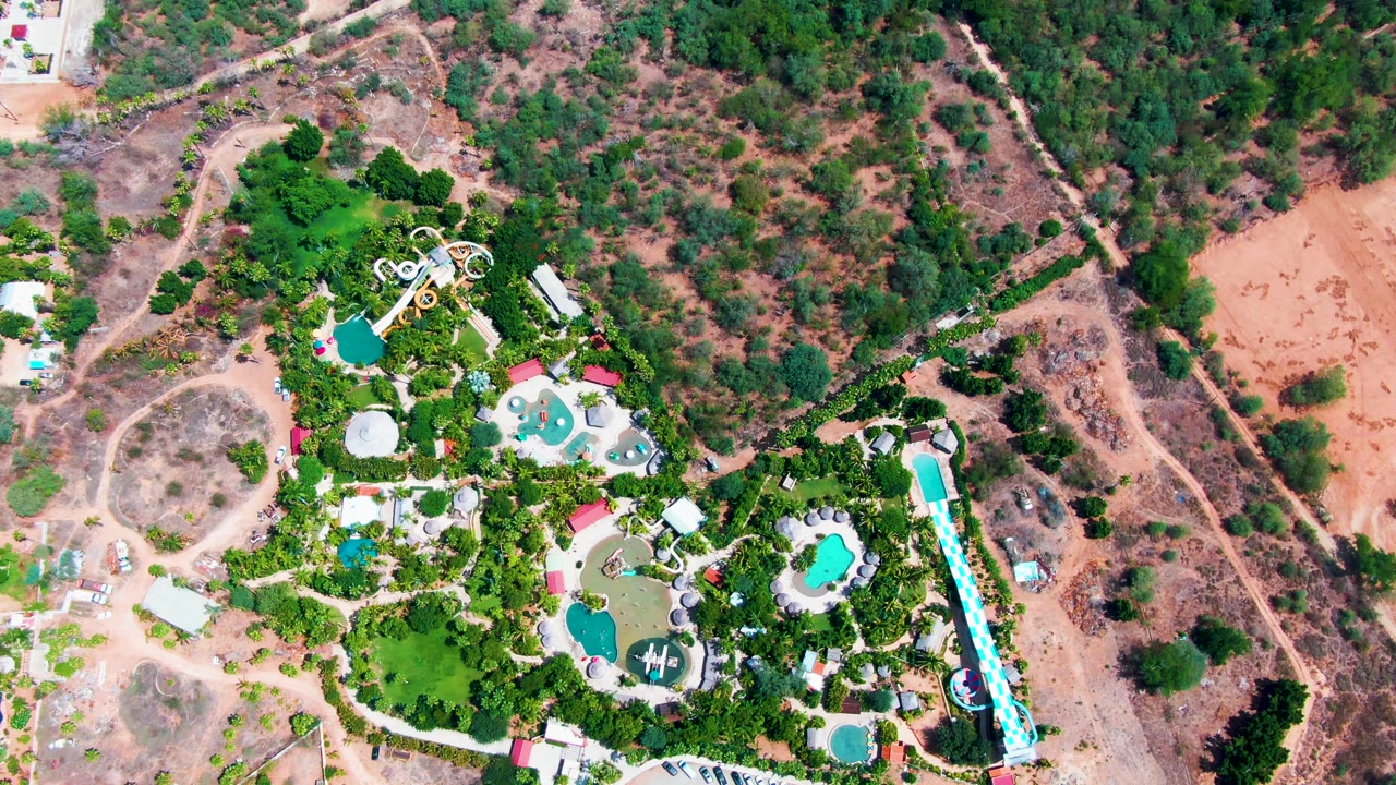 Top-down view in Caduano, Baja California Sur, with the pool area and winding slide near the lower half, dry hillside terrain above and beside it, and no visible people.