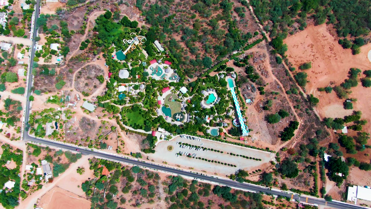 Drone view of a landscaped pool property beside a road and dry land.