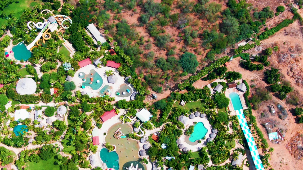A high drone angle over Caduano shows the long turquoise slide lane along the right edge, smaller pools near center, looping slides above, and footpaths through palms.