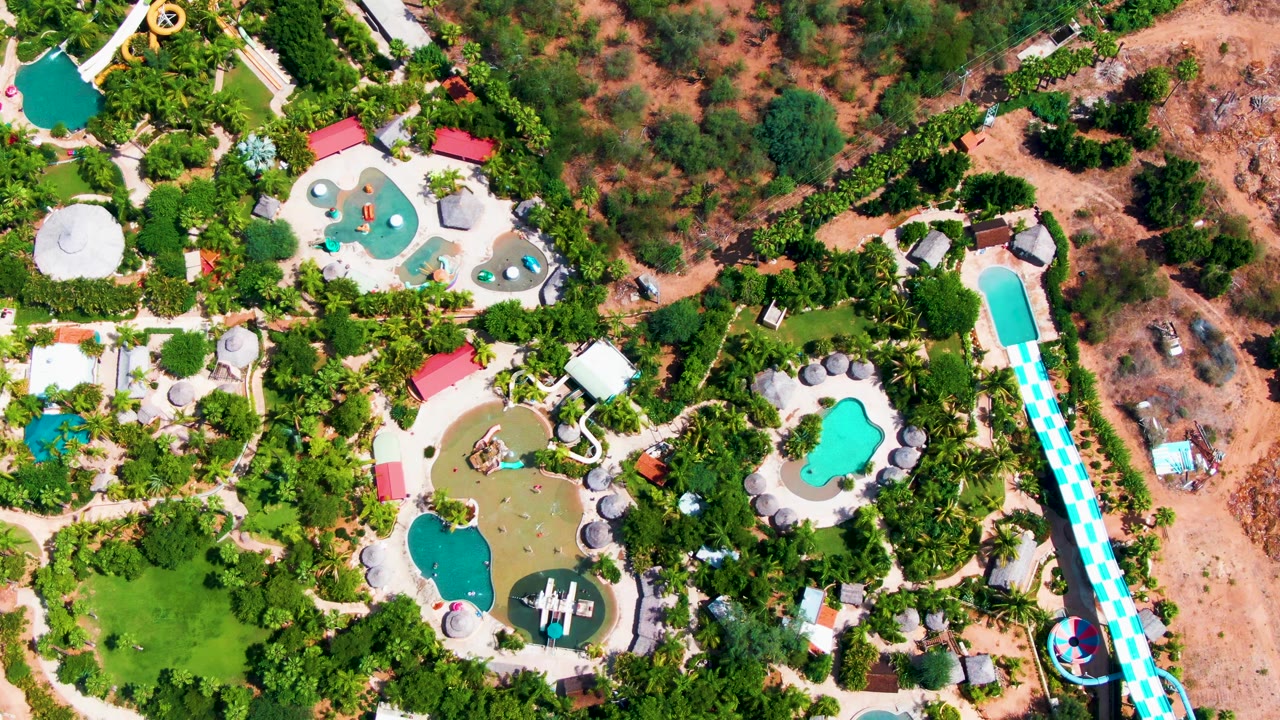 Overhead water park with pools, slides, trees, and dry ground.
