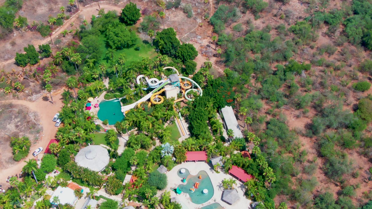 Overhead water park with looping slides, pool areas, palms, and nearby dirt track