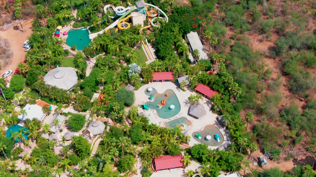 Overhead water park with pools, slides, tropical planting, and dry open ground nearby.