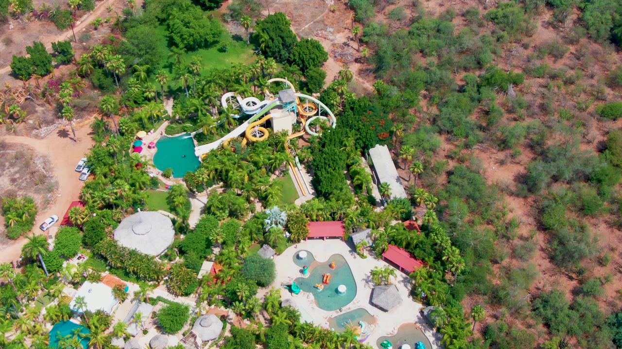 Overhead water park with slide, pools, trees, road, and parked car.