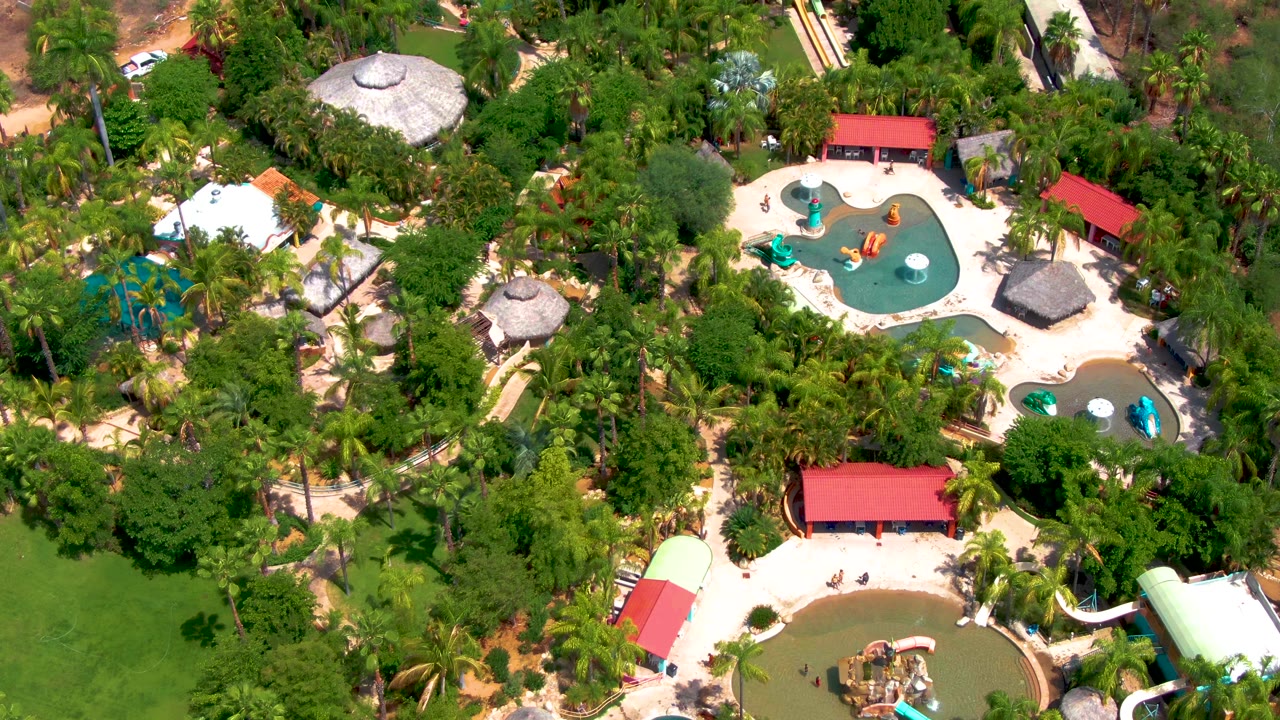 Overhead resort water park with slides, pools, trees, and pale walkways.