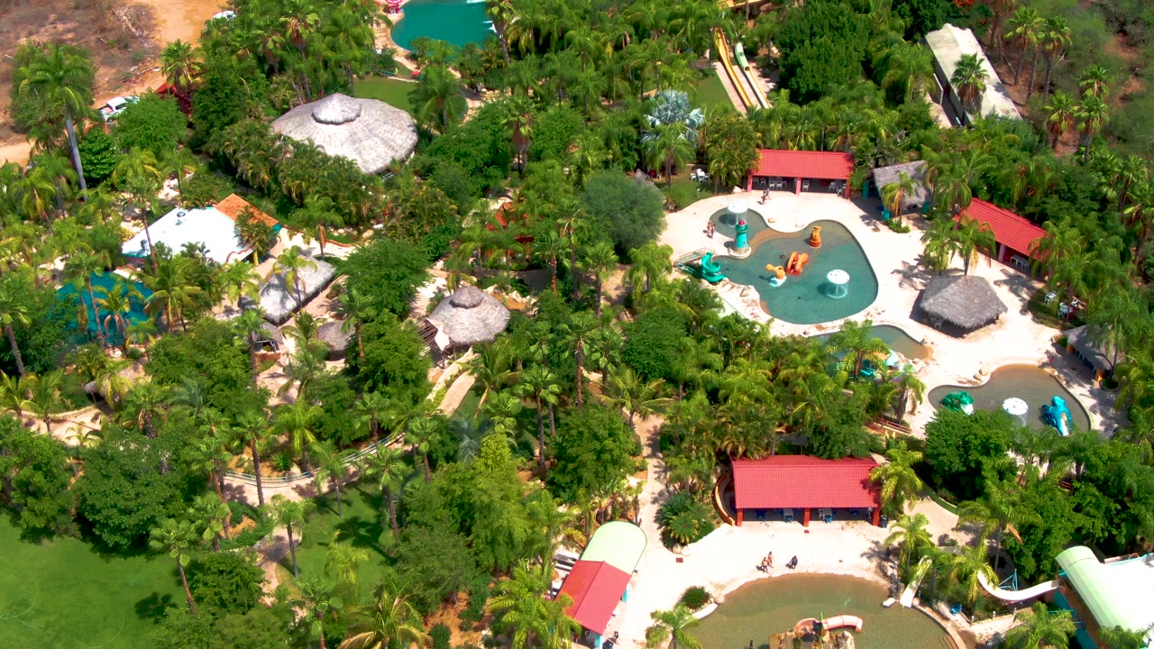 Overhead resort water park scene with pools, huts, trees, and slides.