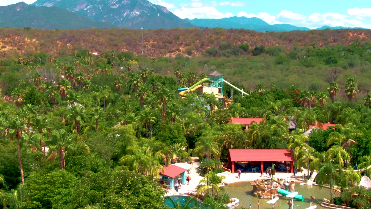 Water park pools and red roofs surrounded by palms with mountains in the distance.