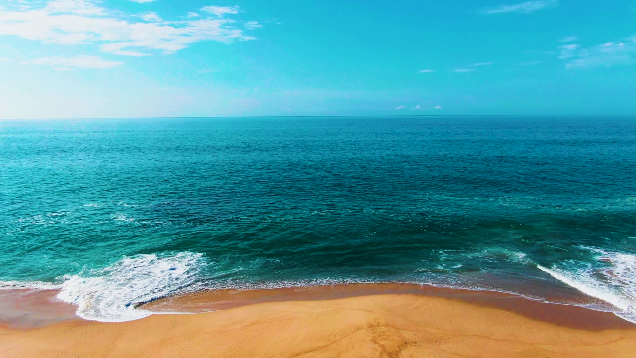 White surf curling farther across the sand beside turquoise water.