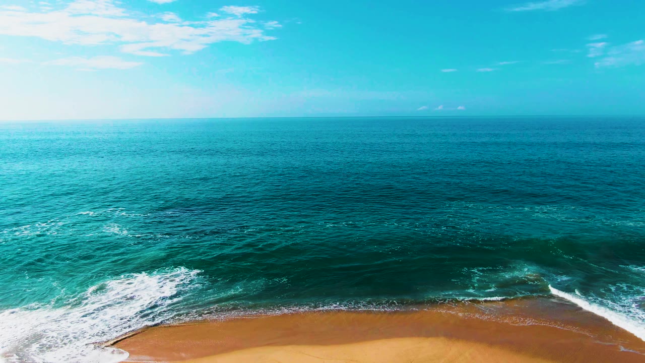 Punta Buzzards shoreline with a diagonal white breaker crossing the lower frame, darker teal water beyond it, and no visible people on the beach or in the water.