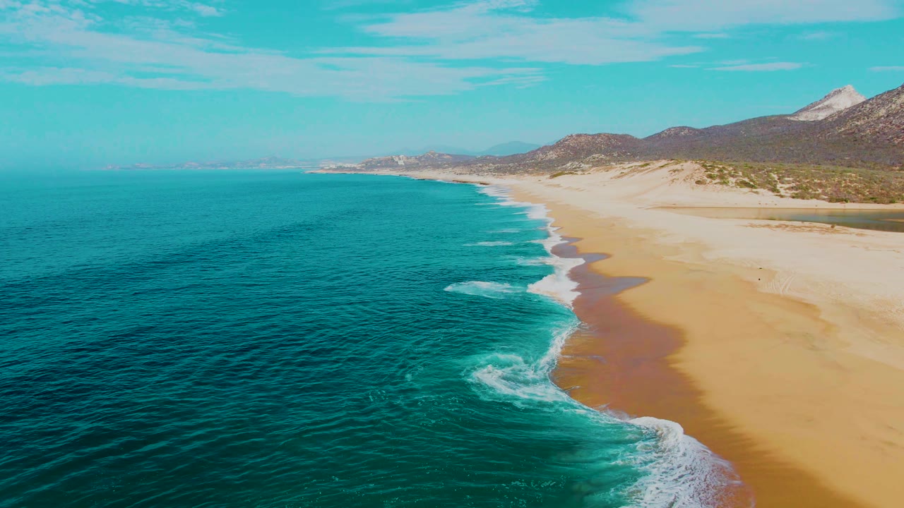 Aerial coastline view with rolling surf, open ocean, and sandy beach.