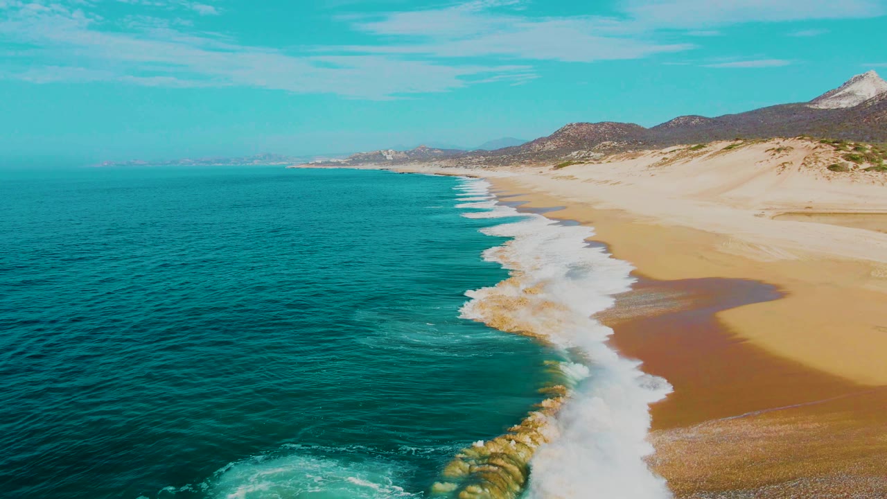 Long sandy beach with parallel white surf lines and turquoise water from above.
