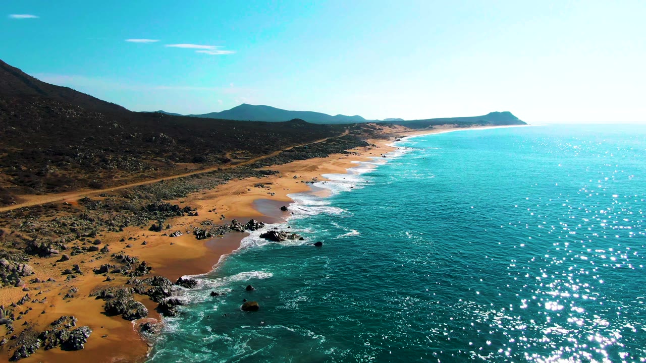 Aerial coastline with beach rocks, road, hills, and ocean
