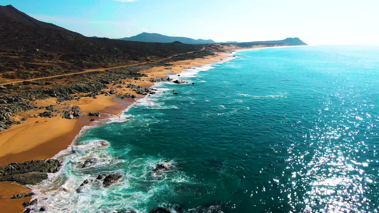 Aerial view of turquoise waves breaking on a sandy rocky coast